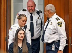 Una madre en silla de ruedas acusada de matar a sus tres hijos es llevada ante el tribunal disadvantage una cruz alrededor del cuello después de que un intento de suicidio la dejara paralizada.